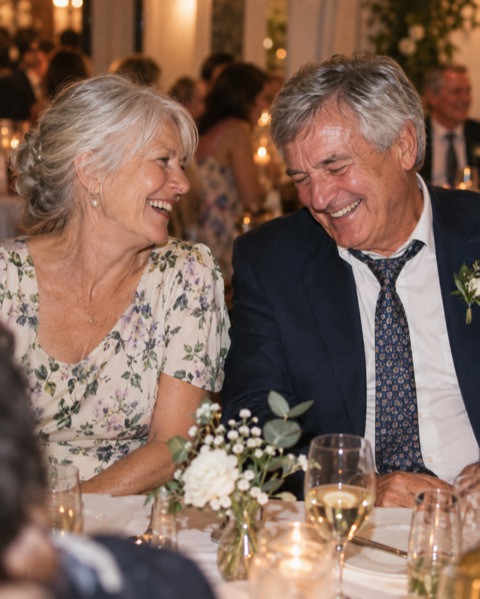 Two older wedding guests sharing a laugh at dinner
